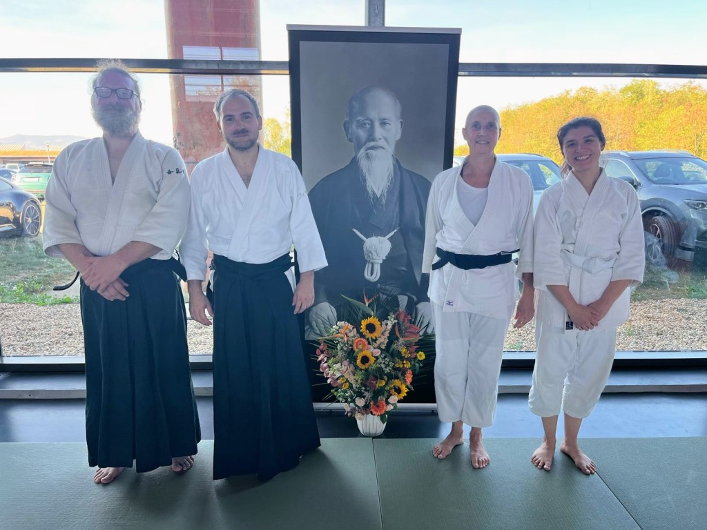 Quatre pratiquants d’AIKIDOJO devant un portrait du fondateur de l’aïkido au Stage de l’amitié à Fareins